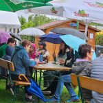 Trotz Regens noch gut besucht Gäste auf Bierbänken mit aufgespannten Regenschirmen